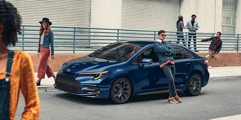 2026 Toyota Corolla Hybrid parked on a city street with people walking by.