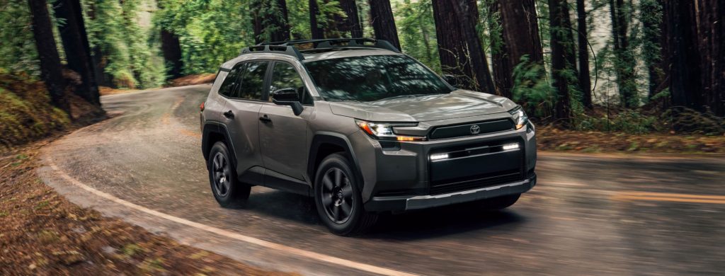 Gray Toyota Crossover SUV driving on a winding road through a forest, showcasing its rugged design and off-road capabilities.