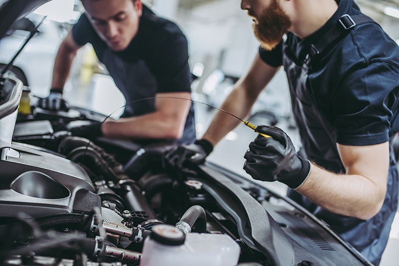 Two mechanics inspecting an engine and checking the oil level.