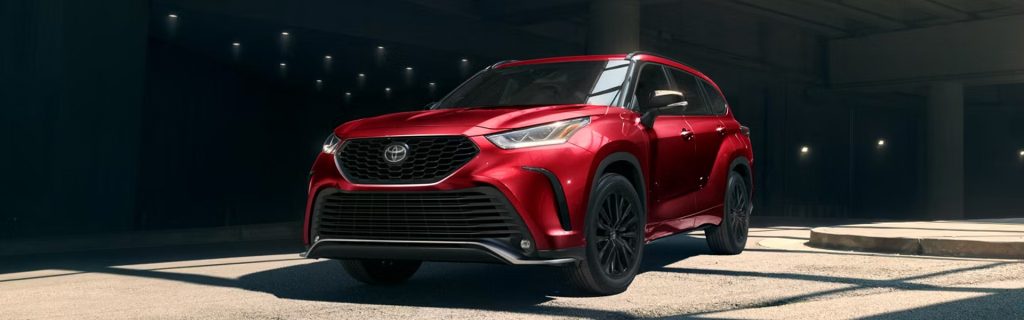 Red 2026 Toyota Highlander parked in a modern, low-light indoor setting with dramatic lighting.